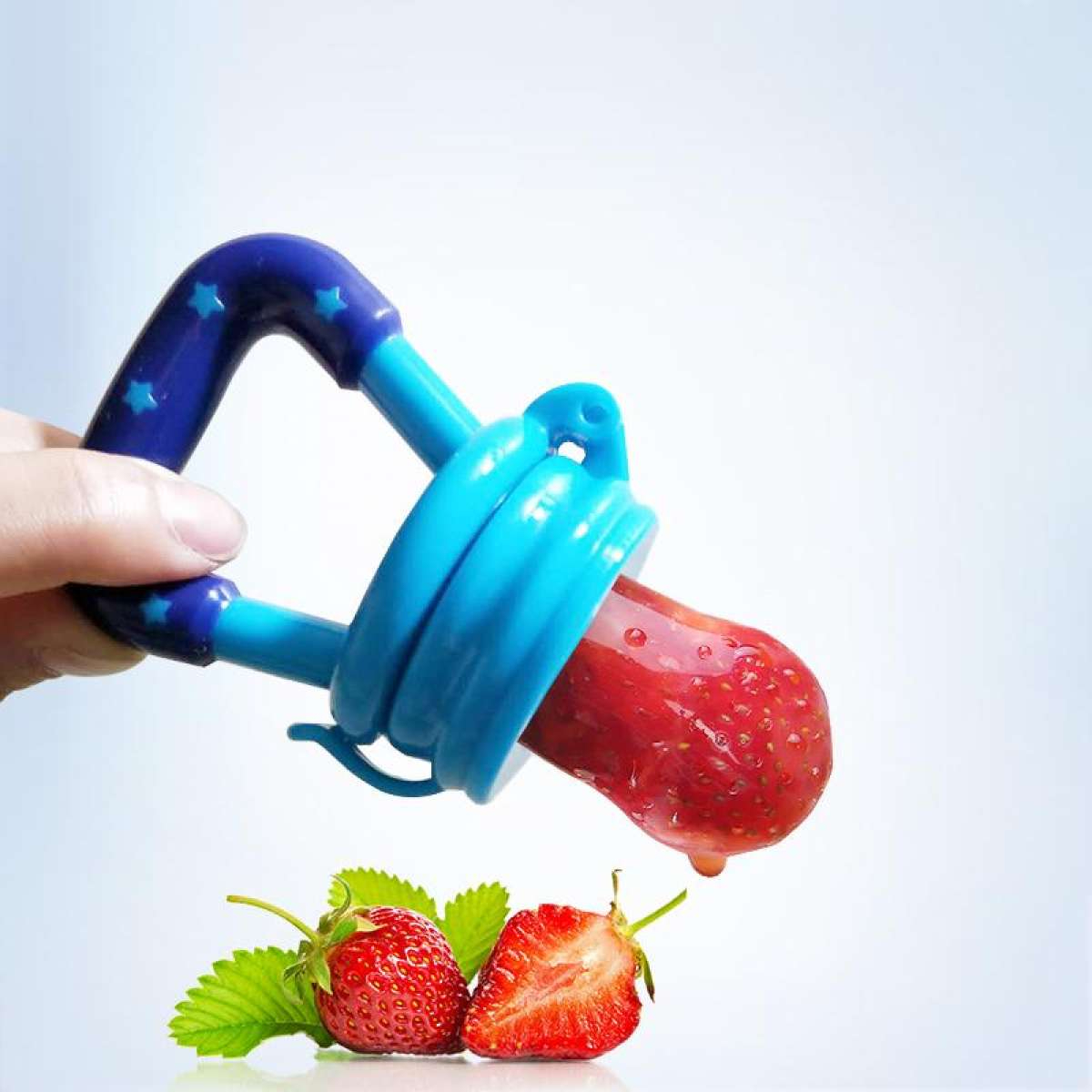 Blue fruit feeder with a strawberry attached, held by a hand on a light blue background.